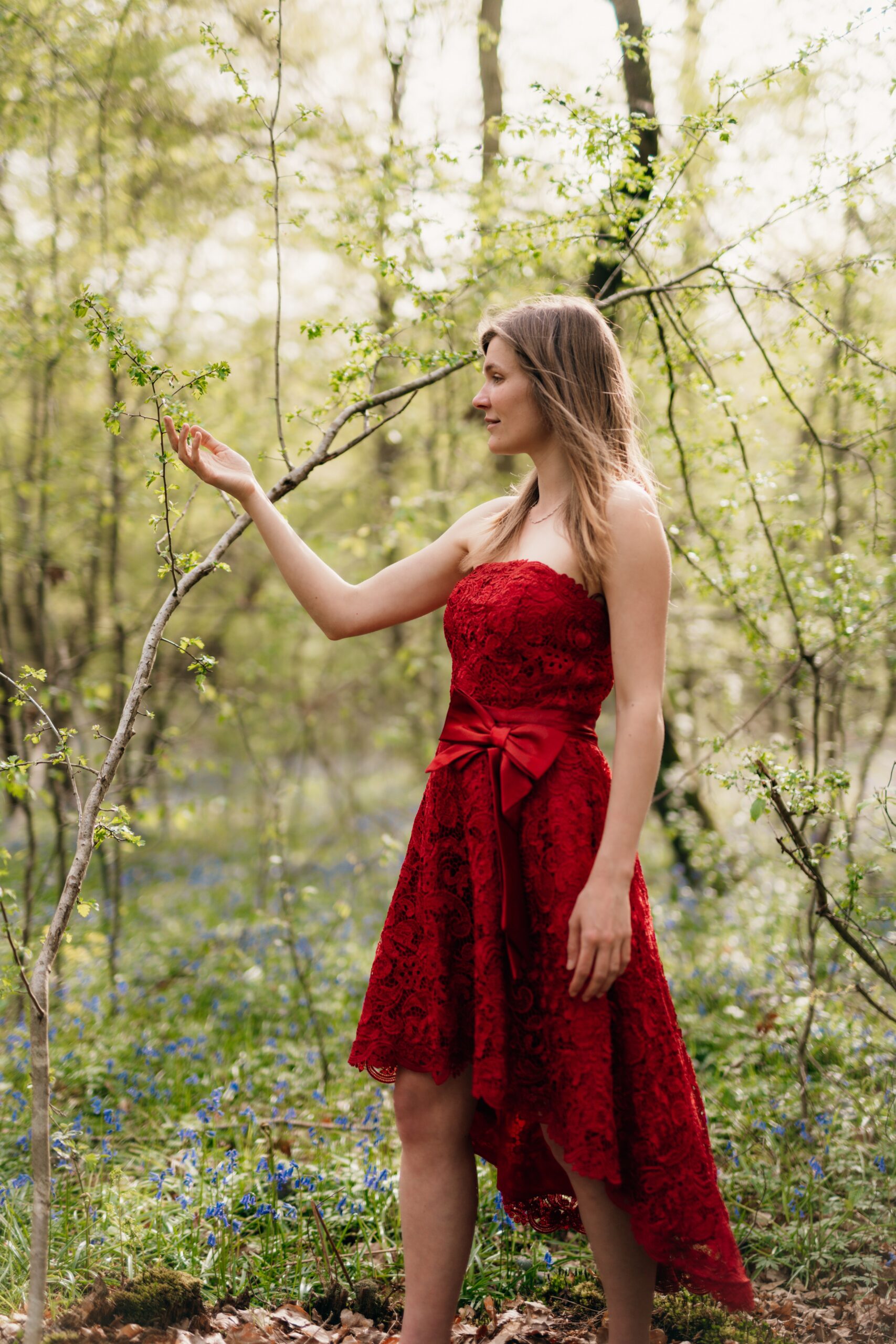 Julia en robe rouge dans la forêt regarde les bourgeons